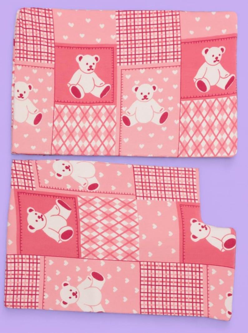 Puede incluir: Dos piezas de tela rectangulares con un patr&oacute;n de patchwork rosa. El dise&ntilde;o incluye cuadrados alternos de ositos de peluche blancos sobre fondo rosa, peque&ntilde;os corazones blancos sobre fondo rosa y un patr&oacute;n de cuadr&iacute;cula a cuadros.