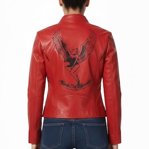 Könnte beinhalten: Rote Lederjacke mit schwarzem Aufdruck auf dem Rücken. Die Grafik zeigt eine geflügelte Frau und den Text "Made in Heaven". Die Jacke hat einen Stehkragen und eine taillierte Silhouette.