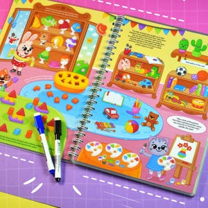 May include: A spiral-bound children's activity book with colorful illustrations. The pages feature drawings of toys, animals, and art supplies. Two markers, one blue and one black, are lying on the open pages. The book has the text "IRMIKA" and "&copy; 2024 Iryna Protsenko / Irmika&reg; All Rights Reserved".