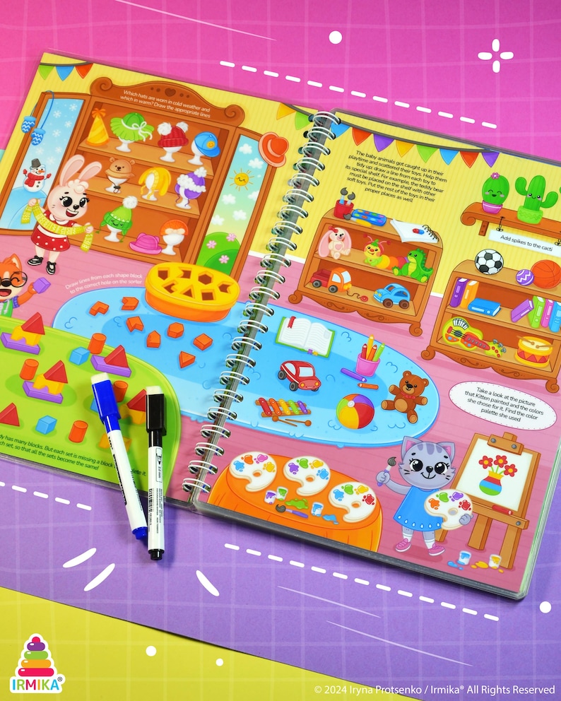May include: A spiral-bound children's activity book with colorful illustrations. The pages feature drawings of toys, animals, and art supplies. Two markers, one blue and one black, are lying on the open pages. The book has the text "IRMIKA" and "&copy; 2024 Iryna Protsenko / Irmika&reg; All Rights Reserved".