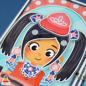 May include: A colorful children's activity set featuring a cartoon girl with black pigtails, wearing a red cap and a blue and white necklace. The set includes various accessories and is designed for creative play. The background has a striped pattern.