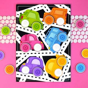 Op de afbeelding: Een kleurrijk kinderspeelgoed met zes speelgoedauto's in verschillende kleuren: groen, oranje, roze, blauw, paars en geel. De auto's zijn geplaatst op een zwart-wit wegontwerp. Extra gekleurde ronde stukken zijn aanwezig.