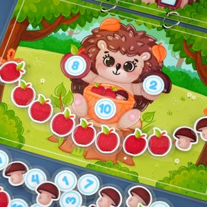 Puede incluir: Un colorido juego educativo con un erizo de dibujos animados sosteniendo una cesta de manzanas rojas. El juego incluye piezas numeradas en forma de manzana y hongo, sobre un fondo de bosque. Los números son del 1 al 10.