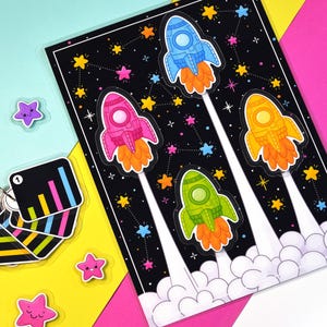 May include: A colorful space-themed illustration featuring four rockets in blue, pink, green, and yellow, ascending from a cloud of smoke against a black starry background. Additional star-shaped stickers and a card with a bar graph are also present.