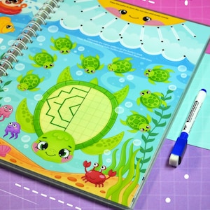 May include: A spiral-bound activity book with a colorful underwater theme. The cover features a large green turtle with a patterned shell, surrounded by smaller turtles, fish, and a crab. A blue and white marker is visible.