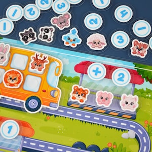Puede incluir: Un colorido juego educativo para niños con un autobús escolar amarillo, pegatinas de animales y fichas numéricas. El tablero del juego incluye una carretera, una parada de autobús y varios personajes de animales. Los números están en círculos blancos.