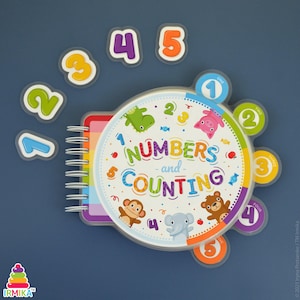 May include: A colorful children's learning book titled "Numbers and Counting" with a spiral binding. The cover features a clock design with numbers and cute animal illustrations. Includes separate number magnets from one to five.