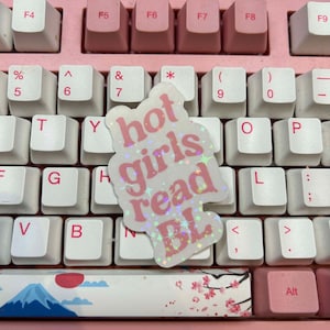 May include: A pink sticker with glitter on a white keyboard. The sticker says "hot girls read BL".