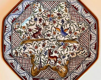 Puede incluir: Un plato de cerámica octogonal con un diseño pintado a mano que muestra un conejo marrón, un pájaro azul y un ciervo rodeados de motivos florales coloridos. El fondo tiene un patrón de rejilla marrón y el borde un diseño de ondas azul y blanco.