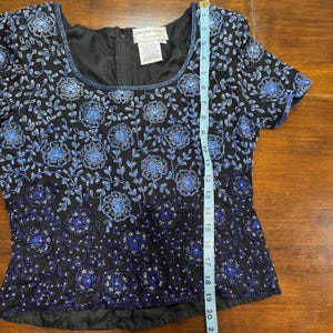 May include: Black short-sleeve top with blue floral beadwork. The top has a square neckline and a zipper in the back. The length of the top is approximately 20 inches.