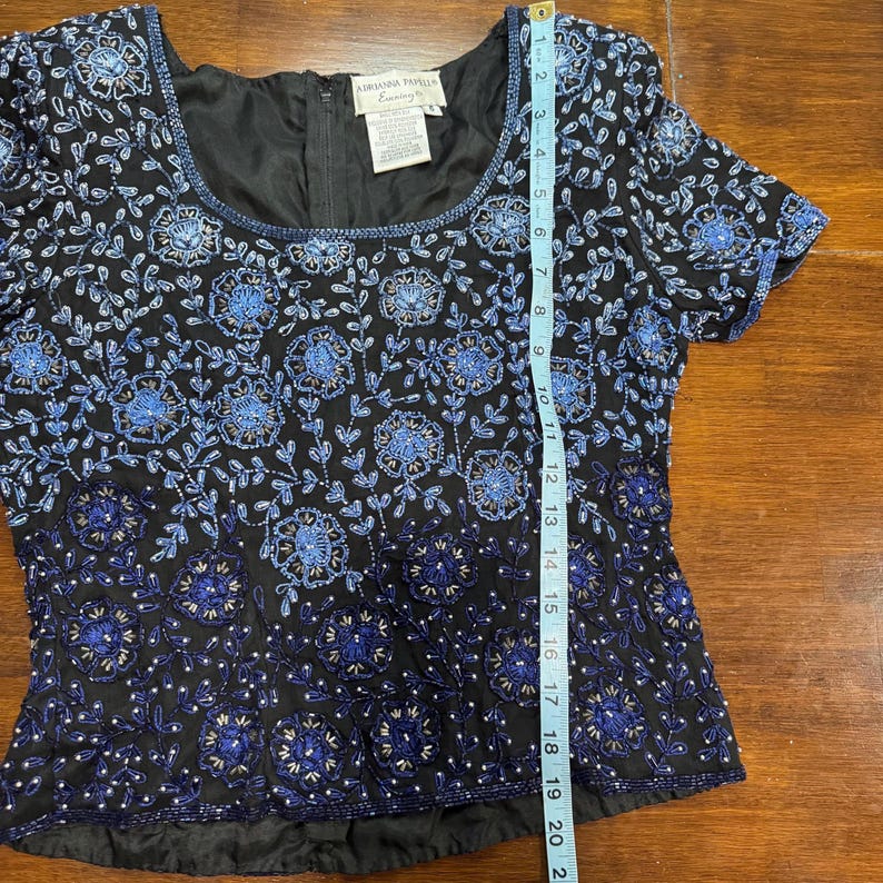 May include: Black short-sleeve top with blue floral beadwork. The top has a square neckline and a zipper in the back. The length of the top is approximately 20 inches.