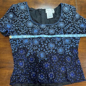 May include: Black beaded evening top with blue floral embroidery. The top has a square neckline and short sleeves. The garment measures approximately 18 inches across the chest. The label reads "Adrianna Papell Evening".