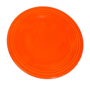 May include: A vibrant orange plate with a circular design. The plate has a smooth, glossy surface and a series of concentric rings near the rim. The plate is a solid, bright orange color, and is set against a white background.