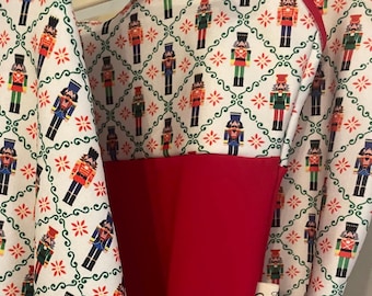 May include: A white sleeveless top and matching skirt featuring a repeating nutcracker pattern in red, green, blue, and black, set against a green diamond lattice design. The top includes a solid red panel and red trim along the neckline.