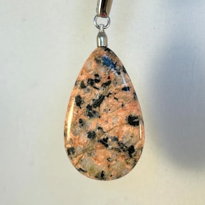 Peut inclure: Un pendentif en forme de larme en granite rose et noir avec une chaîne en argent.