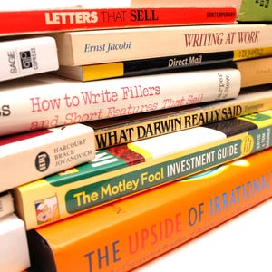 May include: A stack of books with various titles, including "Letters That Sell," "Writing at Work," and "The Motley Fool Investment Guide." The books have different colors and sizes, with visible text on the spines.