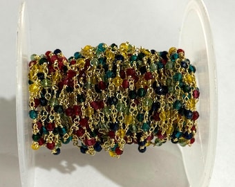 May include: A spool of multi-coloured beaded chain. The chain is made up of small, faceted beads in red, yellow, green, and blue, linked with gold-coloured wire. The beads are closely packed, giving a textured look.