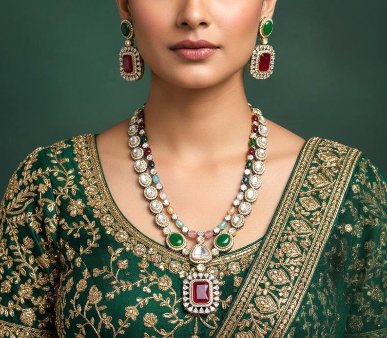 May include: A woman wearing a green and gold embroidered top and a multi-layered necklace with matching earrings. The necklace features a large, square, red gemstone pendant and is adorned with white, green, and other colorful gemstones. The earrings have a similar design.