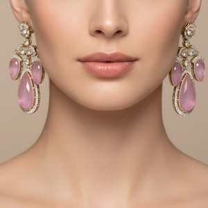 Puede incluir: Elegantes pendientes colgantes con grandes gemas rosas en forma de pera, acentuadas con piedras rosas más pequeñas y cristales transparentes brillantes. Los pendientes tienen un engaste dorado y están diseñados para colgar con gracia.