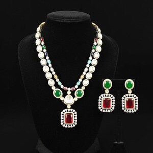 May include: A two-strand necklace and matching earrings set. The necklace features white, green, and red gemstones, with a large red square pendant. The earrings have a similar design, with green and red stones.