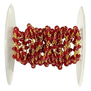 May include: A spool of red beaded chain with gold-colored links. The beads are small, faceted, and a deep ruby red color. The chain is wound around a clear plastic spool, ready for use in jewelry making or other crafts.