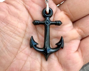 May include: A polished black anchor pendant suspended from a silver-toned metal chain. The anchor features a smooth, glossy finish with a rounded top loop and two curved flukes at the base, attached to the chain by a small silver-toned metal bail.