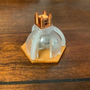 Könnte beinhalten: Ein 3D-gedrucktes Modell eines Gebäudes mit kupferfarbenem Dach und klarer Kuppel. Das Modell steht auf einer orangefarbenen sechseckigen Basis. Das Design des Gebäudes umfasst gewölbte Stützen und eine detaillierte Dachstruktur. Das Modell ist wahrscheinlich eine Miniaturarchitektur.