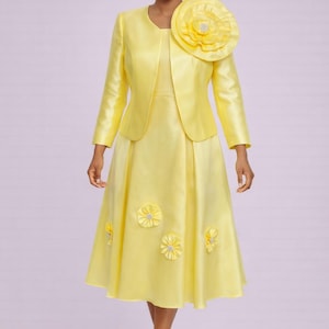 May include: A yellow dress and jacket ensemble. The knee-length dress features floral embellishments and is paired with a matching jacket. A large flower adorns the shoulder. The outfit is completed with yellow heels.