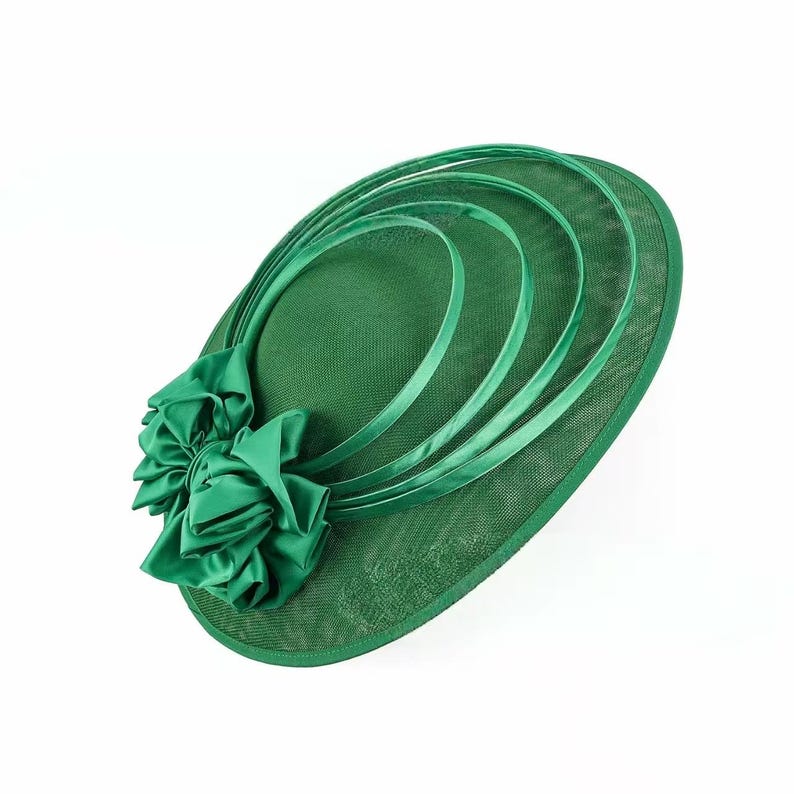 Peut inclure: Chapeau de c&eacute;r&eacute;monie vert avec un large bord et des boucles de ruban d&eacute;coratives. Une grande fleur en satin est attach&eacute;e sur le c&ocirc;t&eacute;. Le chapeau est d'un vert vif uni, adapt&eacute; aux occasions sp&eacute;ciales.