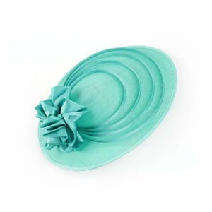 Peut inclure: Chapeau vert menthe avec un grand n&oelig;ud d&eacute;coratif sur le c&ocirc;t&eacute;. Le chapeau pr&eacute;sente un large bord avec des d&eacute;tails ovales concentriques. Le chapeau est de couleur unie et est probablement destin&eacute; &agrave; une occasion sp&eacute;ciale.