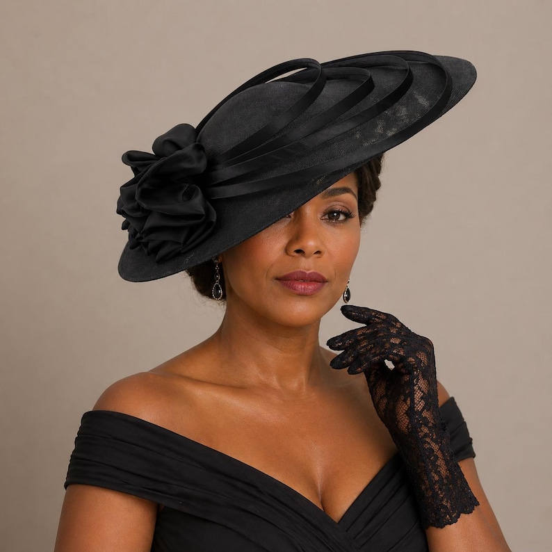 Peut inclure: Un chapeau noir &agrave; larges bords orn&eacute; d'une grande fleur froiss&eacute;e sur le c&ocirc;t&eacute;. Le chapeau est orn&eacute; de rubans noirs. La femme porte des gants en dentelle noire et une robe noire.