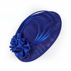Peut inclure: Un chapeau bleu roi avec une grande fleur et des rubans d&eacute;coratifs. Le chapeau a une forme ovale avec une texture en forme de maille et une fleur en satin sur le c&ocirc;t&eacute;. Des rubans courbent le dessus du chapeau.