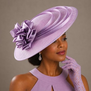 Peut inclure: Un chapeau lavande &agrave; large bord orn&eacute; d'une grande fleur froiss&eacute;e. Le chapeau pr&eacute;sente des rubans superpos&eacute;s et est port&eacute; avec des gants et une robe assortis. Un accessoire de mode &eacute;l&eacute;gant.