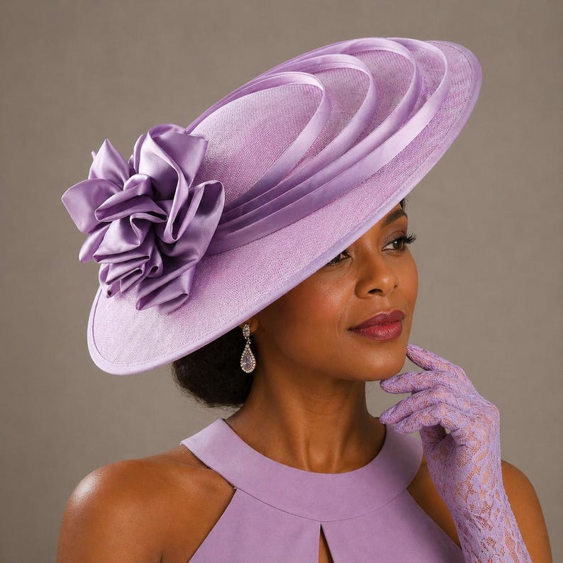 Peut inclure: Un chapeau lavande &agrave; large bord orn&eacute; d'une grande fleur froiss&eacute;e. Le chapeau pr&eacute;sente des rubans superpos&eacute;s et est port&eacute; avec des gants et une robe assortis. Un accessoire de mode &eacute;l&eacute;gant.