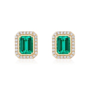 Puede incluir: Un par de pendientes de botón con piedras preciosas verdes de corte esmeralda con un halo de pequeñas piedras preciosas claras engastadas en un metal dorado. Los pendientes se muestran sobre un fondo blanco.