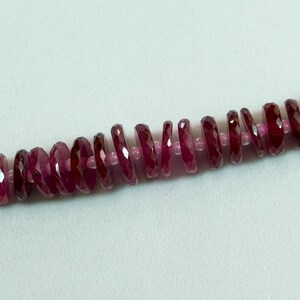Puede incluir: Una hilera de cuentas facetadas en forma de disco de color magenta intenso dispuestas en una fila lineal. Cada cuenta presenta un perfil circular plano con múltiples facetas talladas que reflejan la luz, ensartadas en un cordón fino.