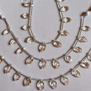 May include: Strands of clear, faceted teardrop-shaped beads with a hint of amber color. The beads are strung on thin, silver-colored wire, with delicate tassel accents in lavender and white. Ideal for jewelry making.