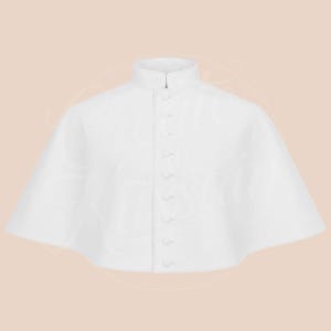 May include: A white cape with a high collar and a row of small buttons down the front. The cape has a slightly flared shape and appears to be made of a smooth, possibly satin-like fabric. The background is a soft, neutral color.