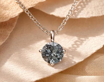 May include: A silver-toned necklace featuring a single round, faceted, slate-gray gemstone pendant held in a four-prong setting. The pendant is suspended from a delicate, thin silver-toned chain with small, uniform circular links that catch the light.