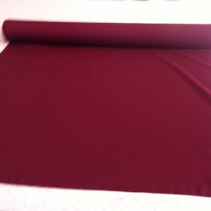 May include: A roll of deep burgundy fabric. The fabric is smooth and has a slight sheen.