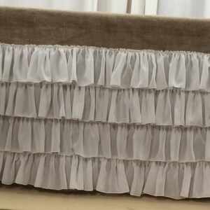 May include: A brown burlap table runner with a white ruffled trim. The trim is made of multiple layers of delicate fabric.