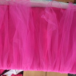 May include: A pink tulle table skirt. The skirt is made of multiple layers of tulle and is gathered at the top. It is a great way to add a touch of elegance to any table.