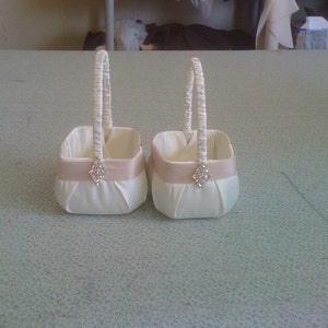 May include: Two white satin flower girl baskets with pink satin ribbon and a rhinestone embellishment.