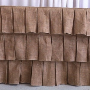 May include: A brown burlap table skirt with three rows of ruffles. The skirt is made of a natural fabric and has a rustic look.