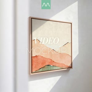 Puede incluir: Una pieza de arte mural cuadrada enmarcada que presenta un paisaje abstracto con colinas en capas en tonos crema, melocotón, terracota y verde apagado. La obra está en un marco de madera clara con el texto VIDEO MOCKUP sobre la imagen.