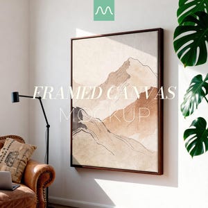 May include: A square framed canvas featuring an abstract mountain landscape in shades of beige, tan, and brown with thin black line art details. The artwork is displayed on a white wall, with the text FRAMED CANVAS MOCKUP overlaid in white.