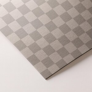 May include: A close-up of a gray and light gray checkered pattern. The pattern is made up of squares and is slightly textured. The surface is angled, with a white background.