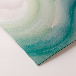 May include: Close-up of a textured surface with a watercolor design. The artwork features soft gradients of teal, green, and pale pink, creating a serene and abstract composition. The corner of the artwork is visible, showing the edge of the canvas.