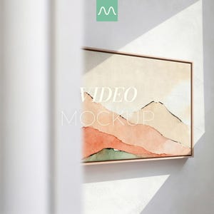 Può includere: Una stampa su tela incorniciata con un paesaggio montano ad acquerello nei toni del pesca, rosa e verde. L'opera d'arte è esposta su una parete bianca, con le parole "VIDEO MOCKUP" sovrapposte. La cornice è di colore marrone chiaro.