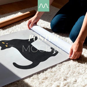 May include: A poster mockup featuring a black cat illustration with yellow eyes. The poster is being unrolled on a white rug. The text "POSTER MOCKUP" is visible on the poster. A rolled-up poster is in the background.